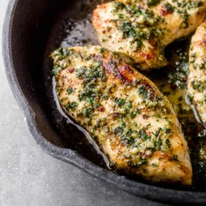 Garlic herb chicken breasts sizzling in a cast iron skillet.