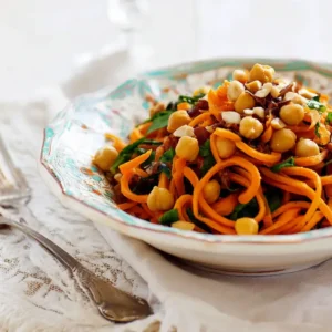 Carrot ribbon salad with crispy roasted chickpeas, chopped walnuts, and fresh parsley served in a decorative bowl