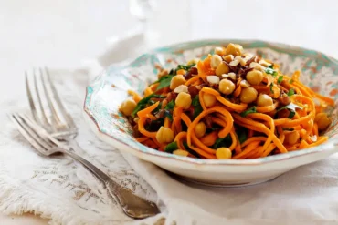 Carrot ribbon salad with crispy roasted chickpeas, chopped walnuts, and fresh parsley served in a decorative bowl